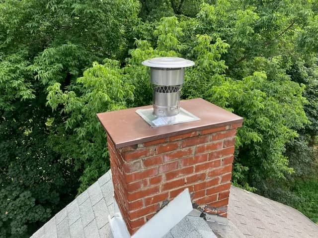 Brick chimney with a copper-colored top plate and stainless steel chimney cap.